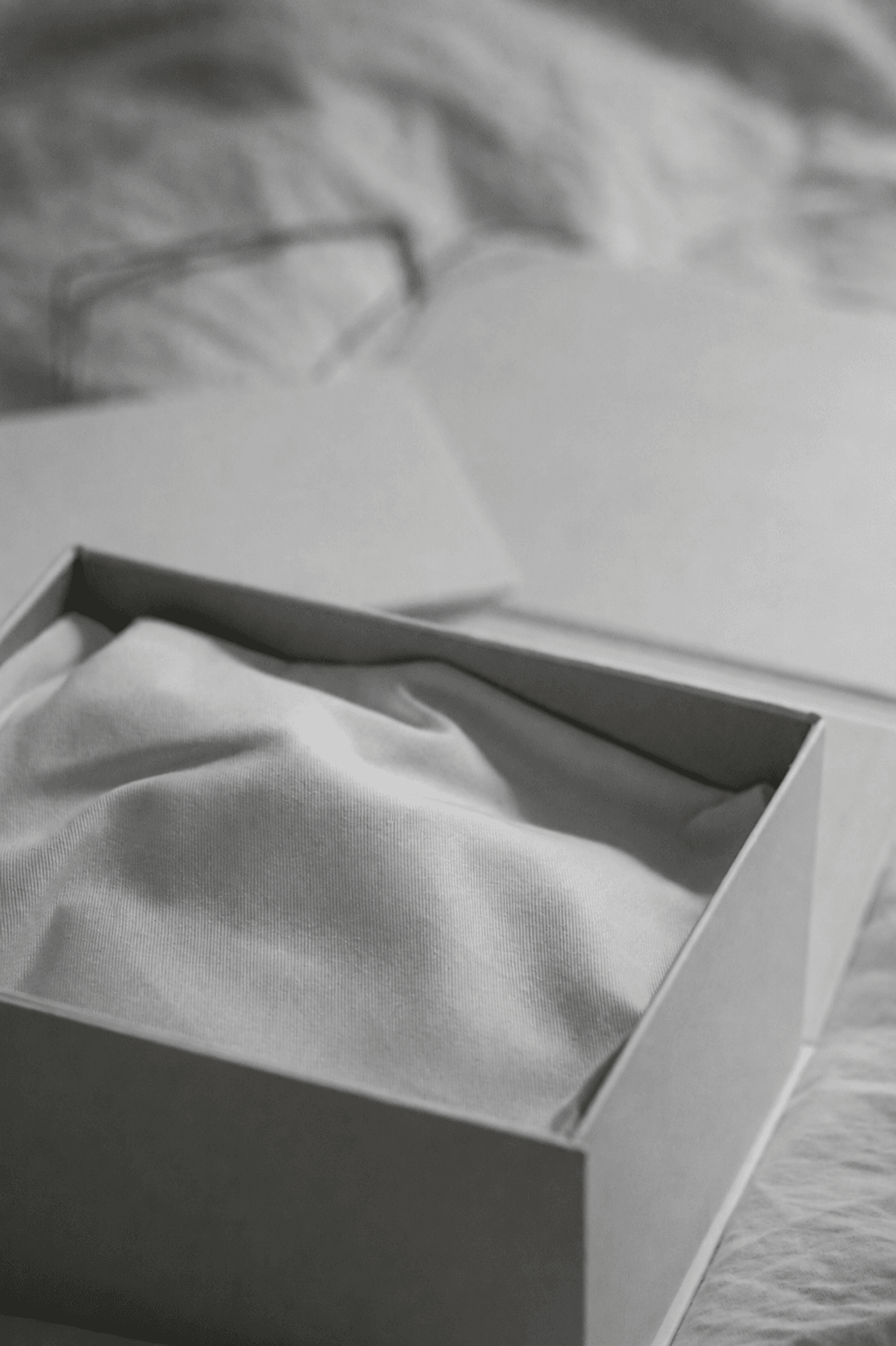 Caja de regalo abierta sobre una cama hecha en blanco y negro editorial